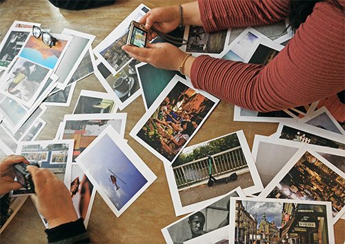 print out of images on a table with hands of two women holding a compact camera